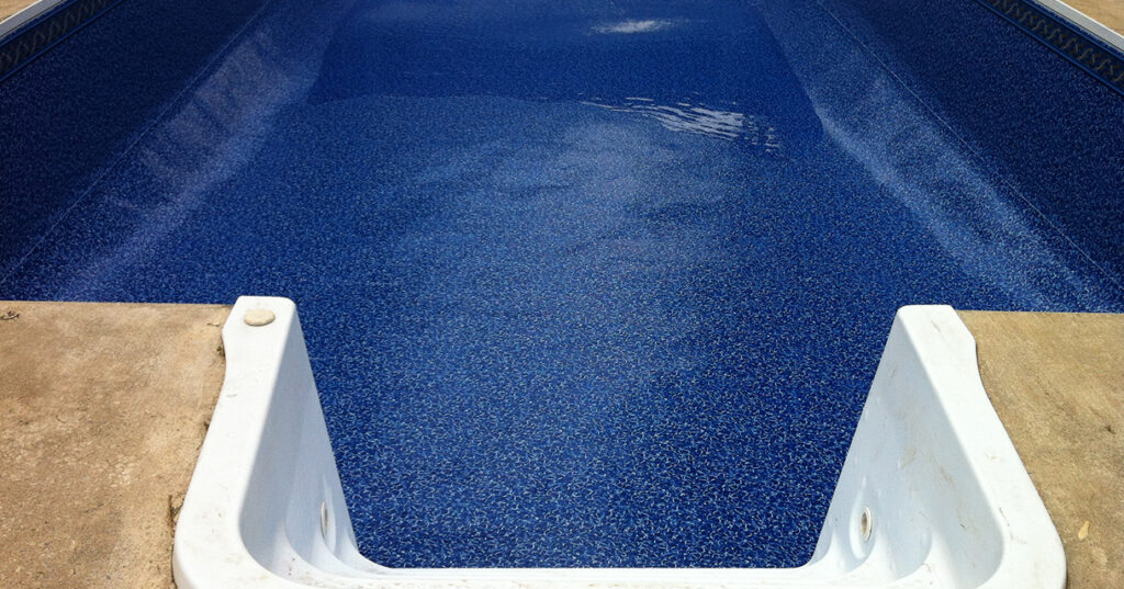 Empty inground swimming pool with blue textured liner and white steps.
