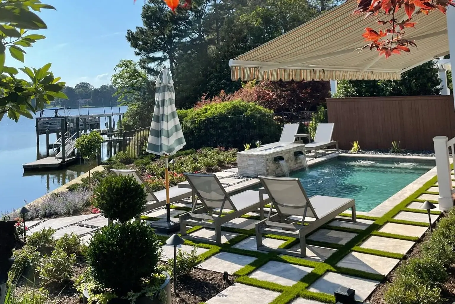 Small luxury backyard pool with lounge chairs overlooking a lake.