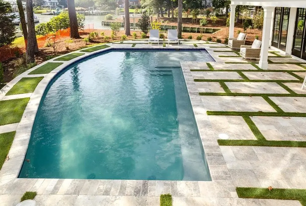 Modern inground swimming pool with travertine pavers and turf patio.