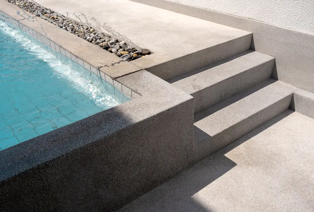 Concrete stairs leading to a swimming pool with a water fountain feature.