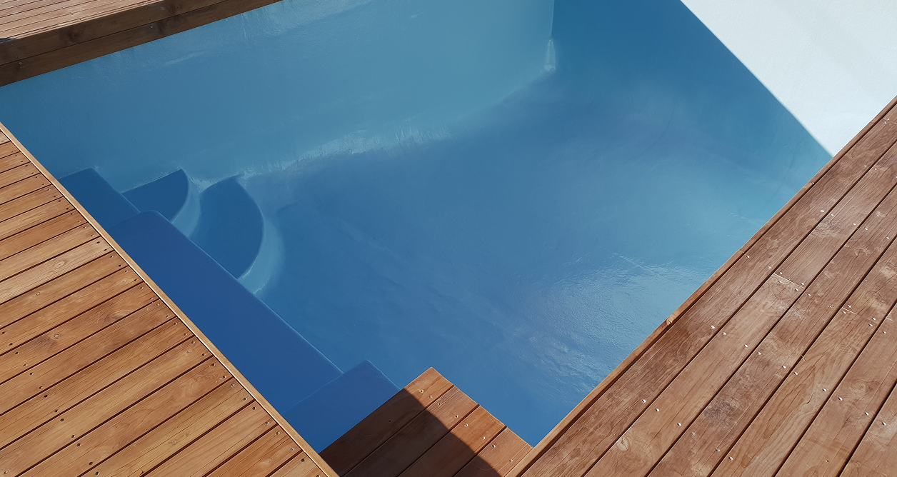 Modern blue swimming pool with integrated steps and a surrounding wooden deck.