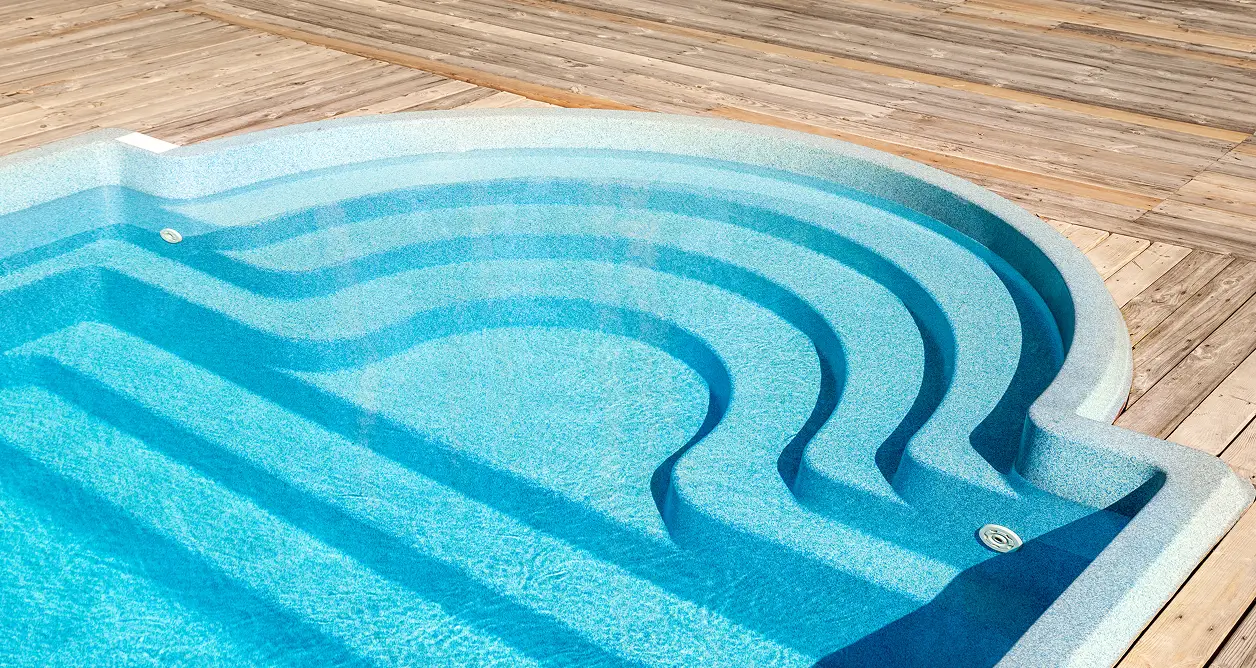 Blue fiberglass swimming pool with unique curved walk-in steps integrated into a wooden deck.