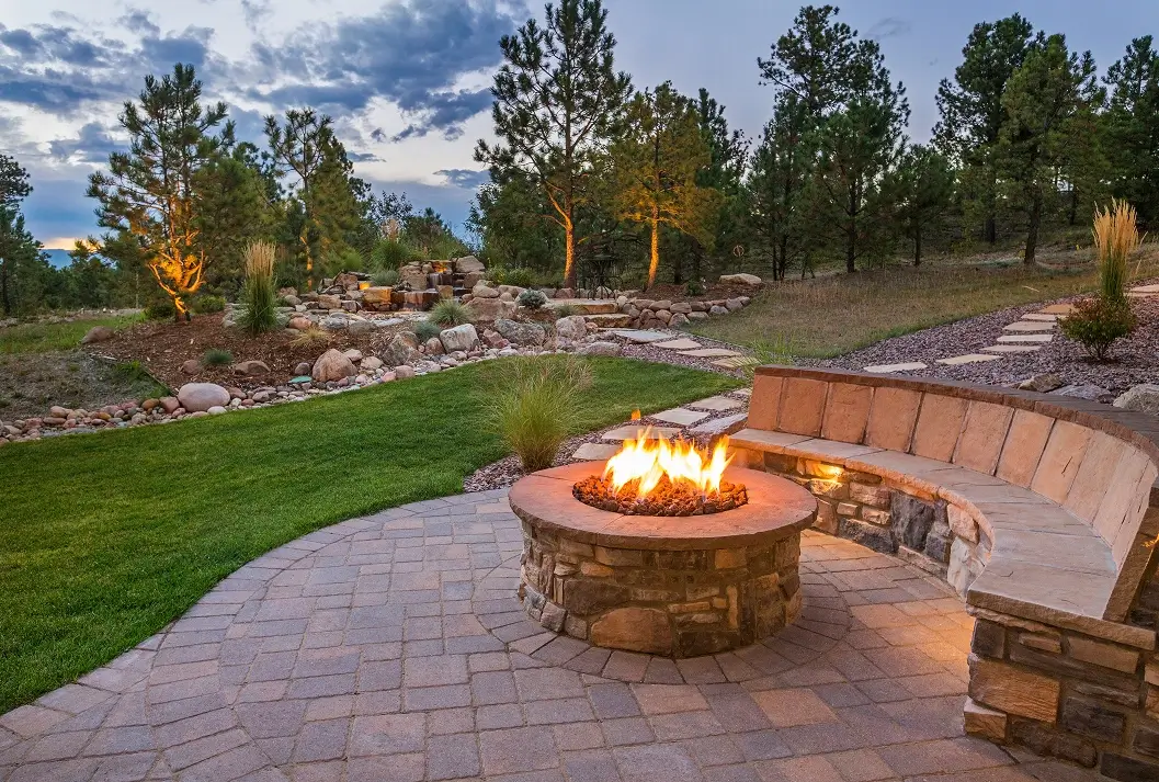 Round stone fire pit with built-in curved bench seating on a paver patio.
