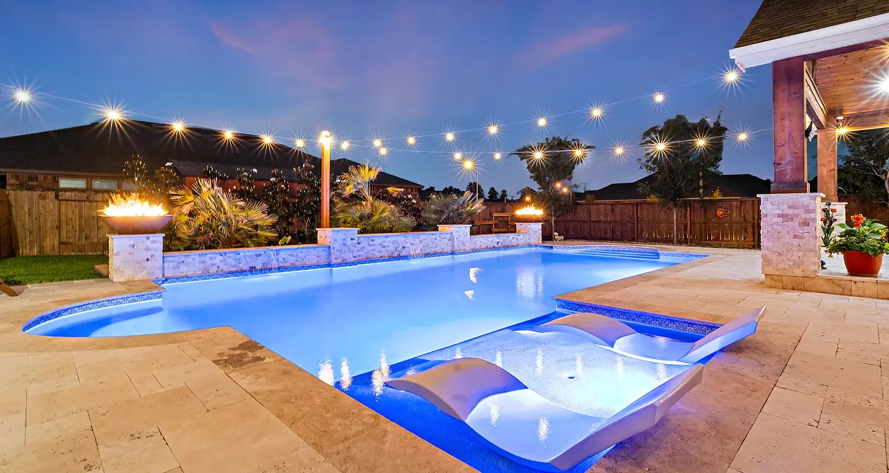 Swimming pool at dusk with blue underwater lights, fire bowls, and string lights.