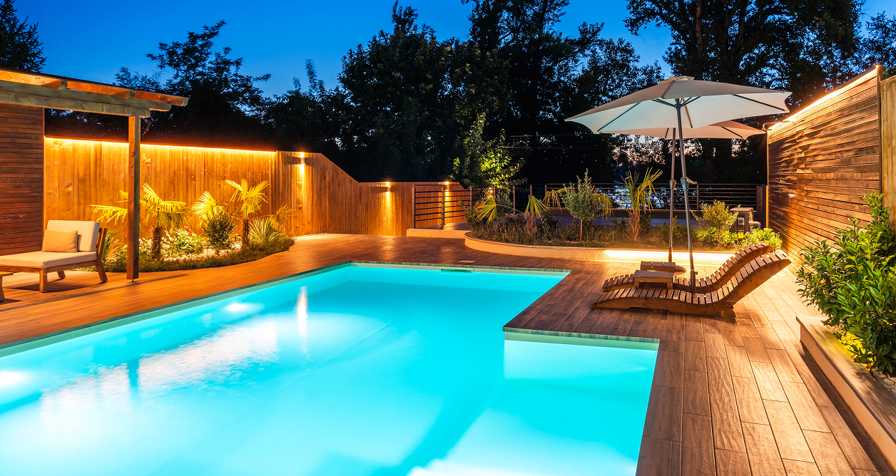 Modern illuminated pool and wood deck with integrated architectural landscape lighting.