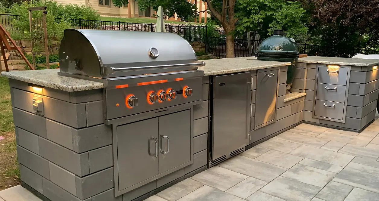 Modern outdoor kitchen with stainless steel grill, kamado smoker, and granite countertop.