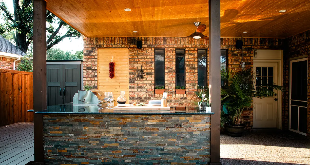Covered patio outdoor kitchen bar with stacked stone veneer and wood ceiling.