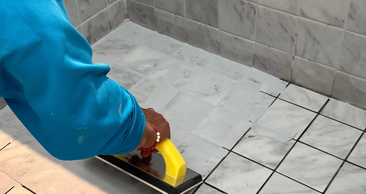 Worker applying grout to marble tiles with a trowel.