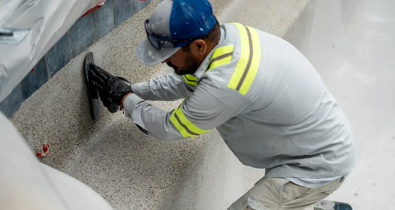 Worker smoothing out gray plaster finish on a pool wall.