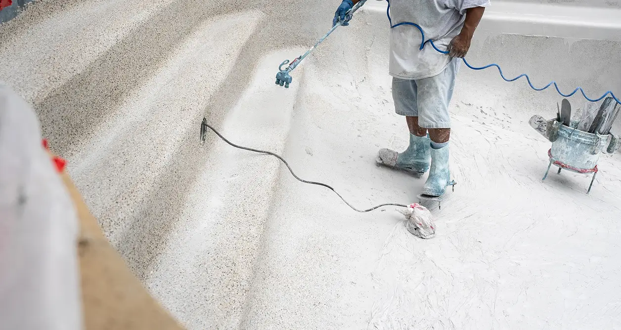 Worker applying fresh white plaster finish to pool steps during pool resurfacing.
