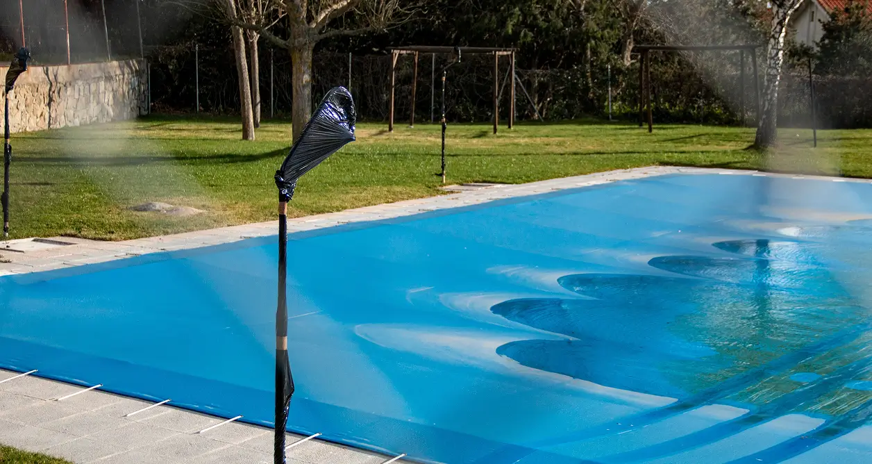Bright blue protective safety cover secured over a backyard outdoor swimming pool.