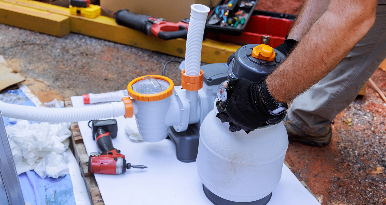 Technician installing a sand filter system for an above-ground swimming pool.
