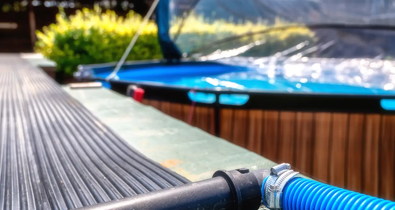 Blue plumbing hose securely clamped to black piping next to an above-ground pool.