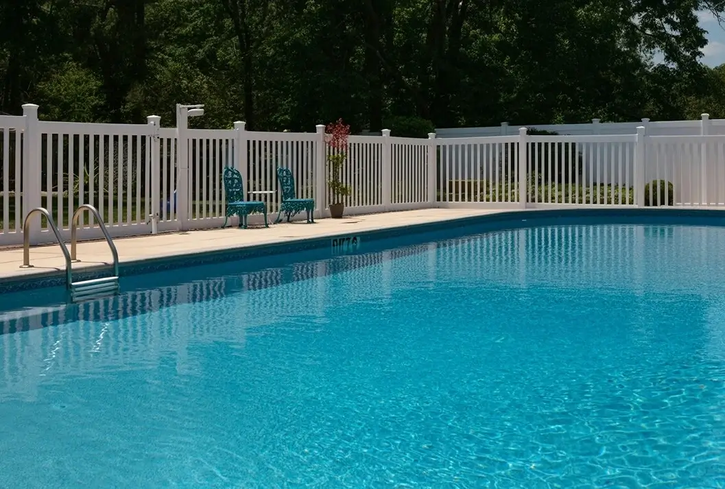 Large vinyl liner pool enclosed by a white safety fence in a backyard.