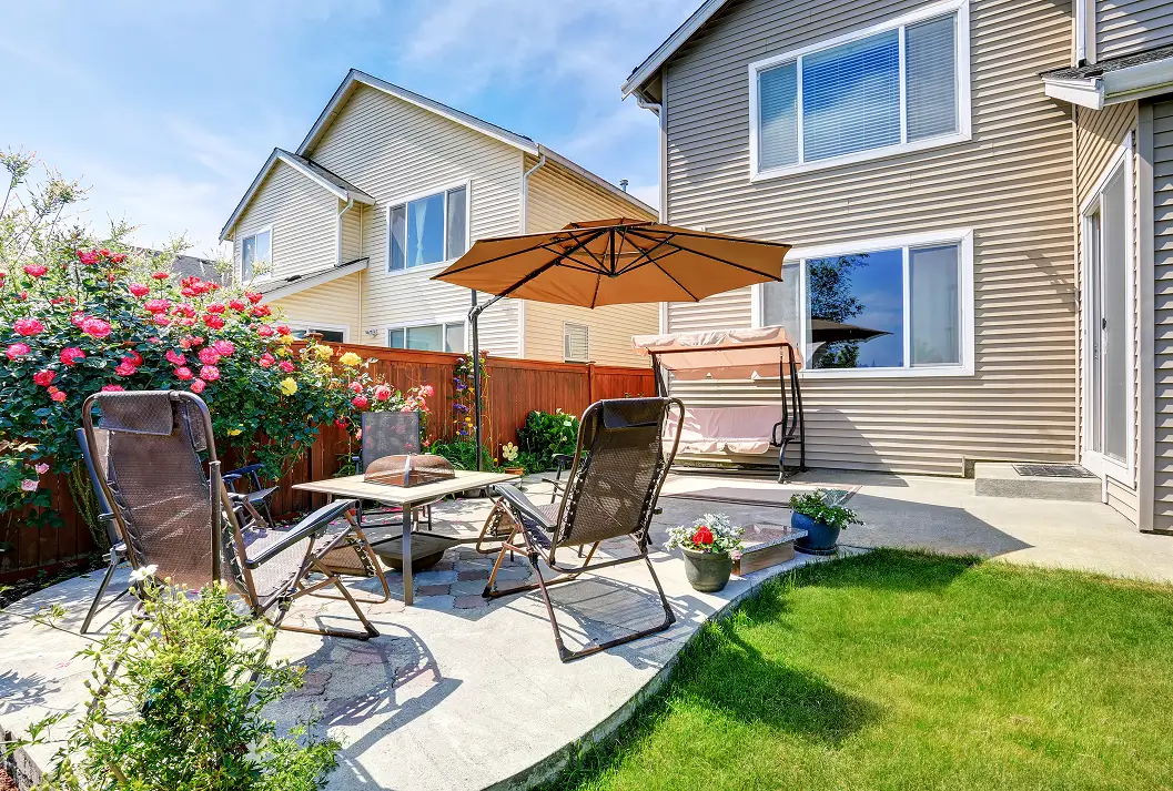 Backyard concrete patio with lounge chairs, umbrella, and rose bushes.