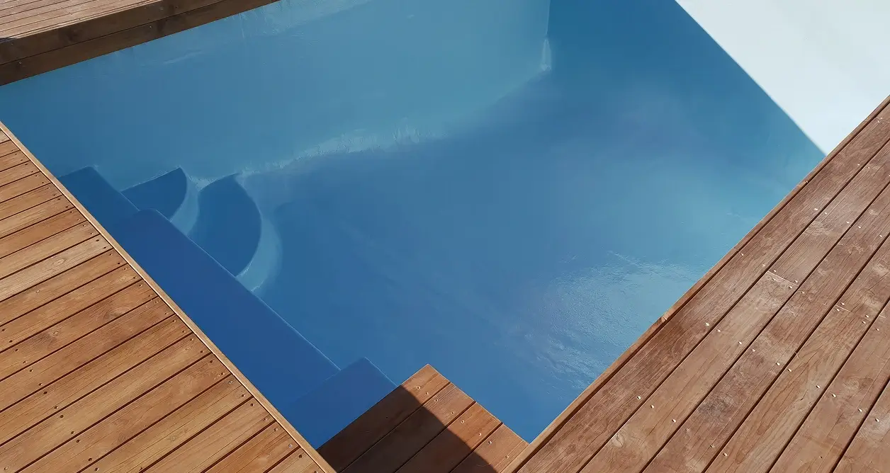 Blue fiberglass swimming pool with corner steps surrounded by a wooden deck.
