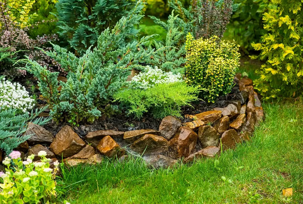 Low natural stone border wall separating a garden bed from green grass.